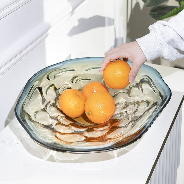 Hand placing orange into large wavy glass fruit bowl