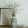 Green and blue ceramic floral vase with branches on table