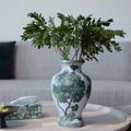 Green floral ceramic vase styled on coffee table with leaves