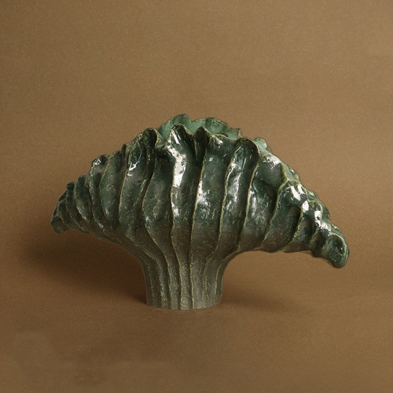 Front view of green glazed ceramic scalloped shell vase against brown background