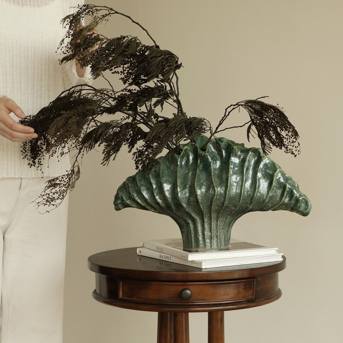 Lifestyle shot of green ceramic shell vase with dried botanicals on wooden table