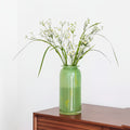 Green glass vase with flowers on wooden table