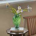 Green swirl art glass vase with iris flowers on table