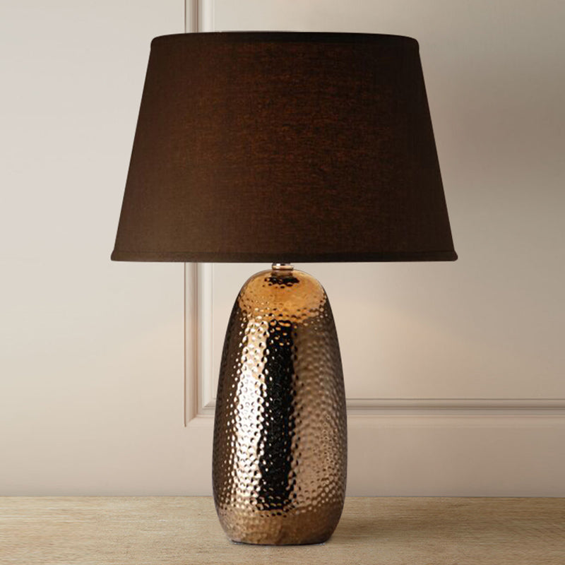 Hammered bronze ceramic lamp lit up against white wall