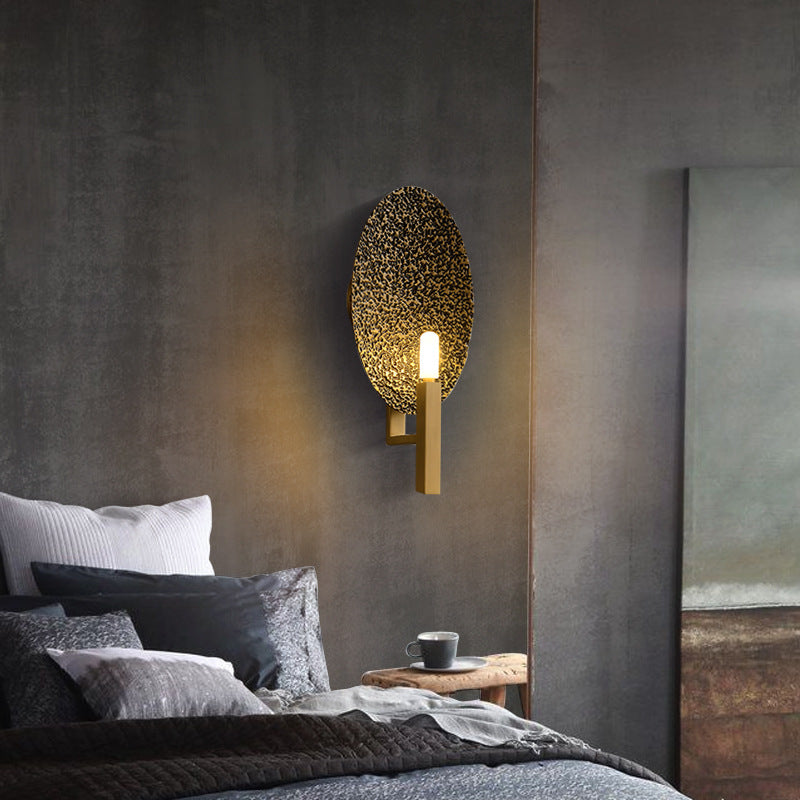 Hammered copper oval wall sconce illuminated in modern bedroom