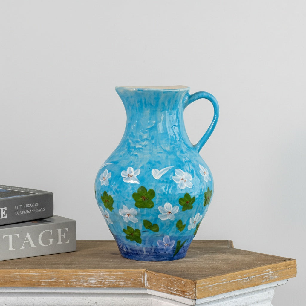 Front view of hand-painted blue ceramic pitcher with white floral design