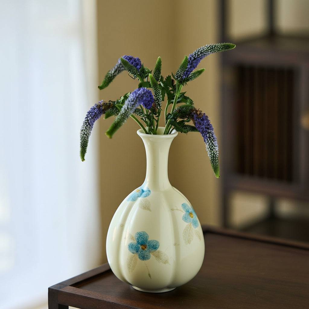 Cream ceramic vase with blue flowers holding purple stems