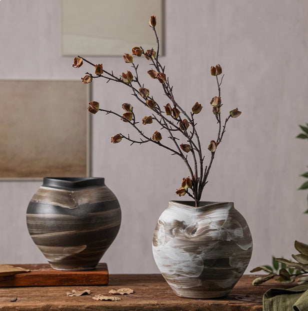 Two textured ceramic vases with dried flowers on wooden table