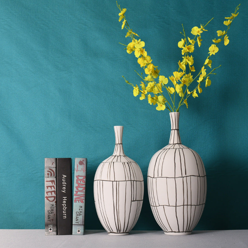 Two white ceramic vases with black lines styled with yellow flowers and books
