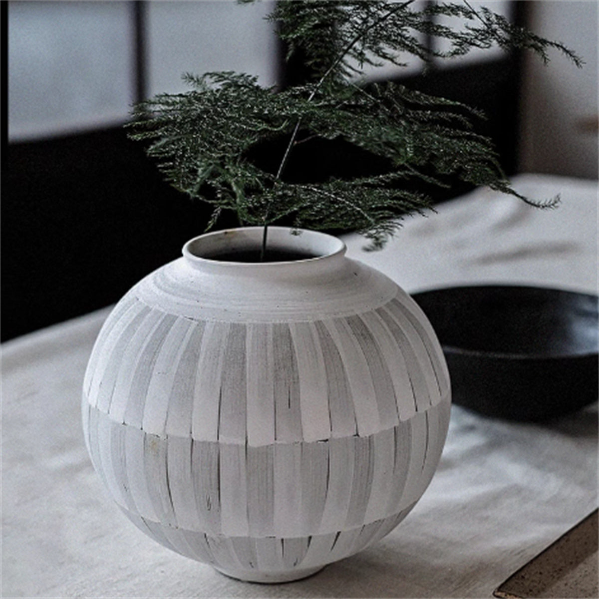 Textured ceramic vase with fern on linen tablecloth