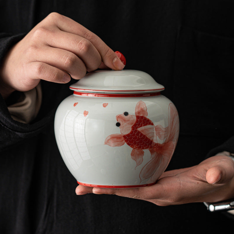 Red goldfish ceramic tea caddy jar held by hand with lidded storage design