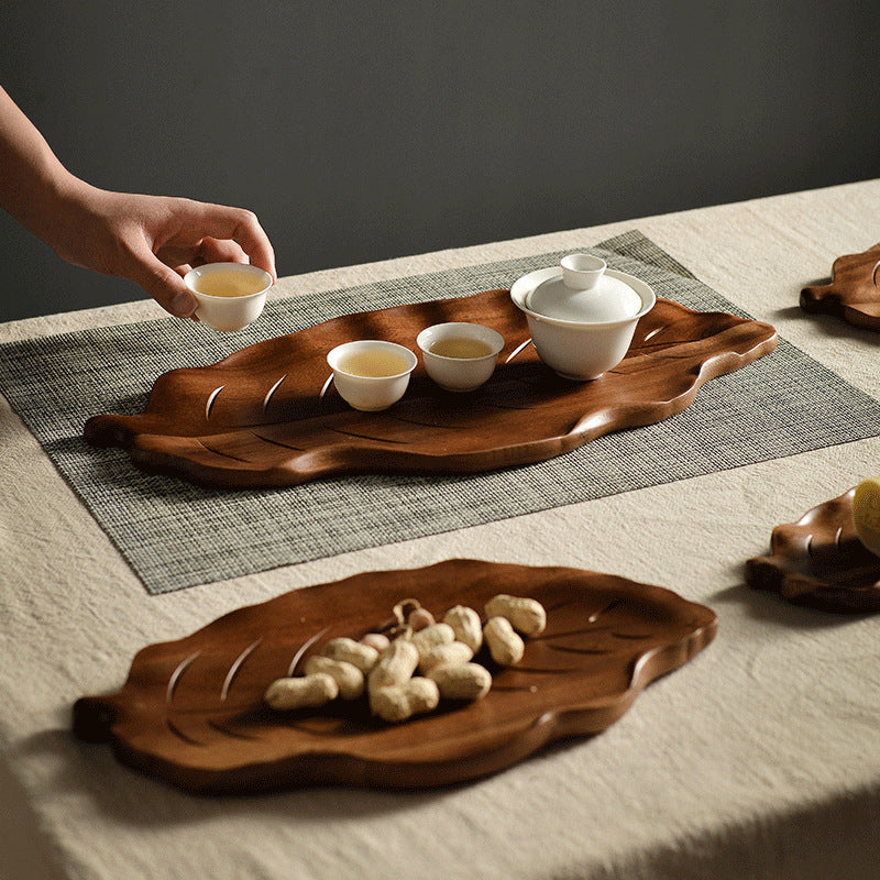Wooden leaf serving platter holding a white ceramic tea set and cups for a tea ceremony