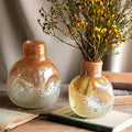 Iridescent amber glass round vase with dried flowers on wooden table