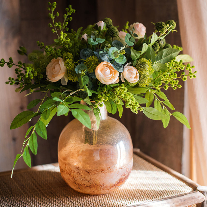 Amber glass vase filled with greenery and roses on rattan surface