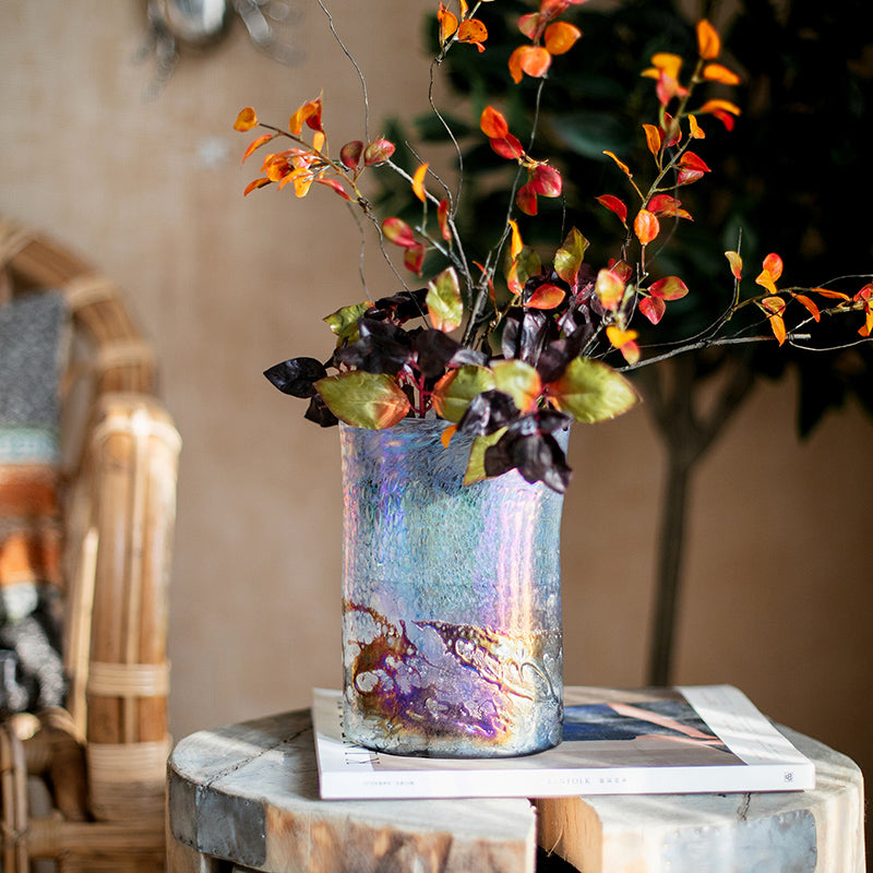 Medium iridescent cylindrical vase with autumn leaves on a wooden stool