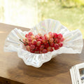 Iridescent white glass ruffled bowl with red grapes on wooden table