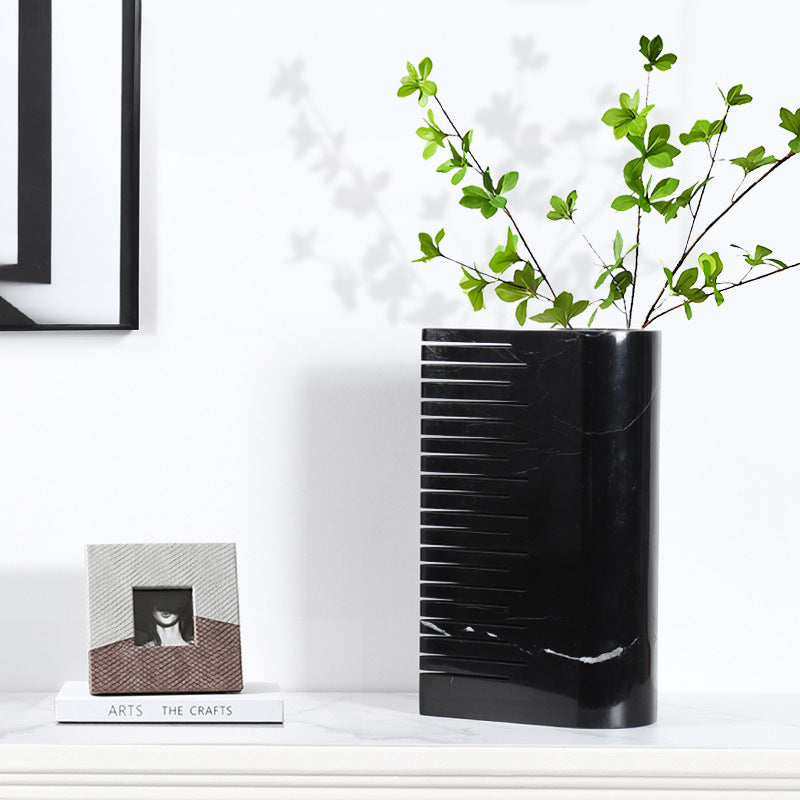 Large black marble vase styled with green branches showing dramatic white veining