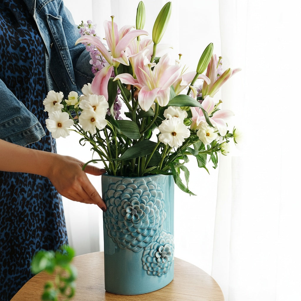 Person arranging a floral bouquet in a light blue ceramic vase