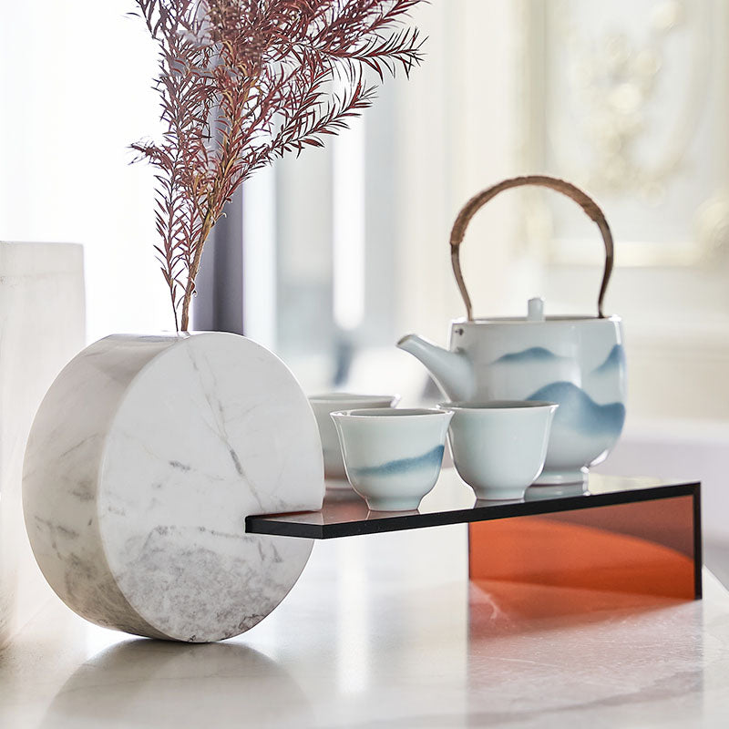 Lifestyle shot of round marble vase holding dried branch next to ceramic tea set on amber shelf