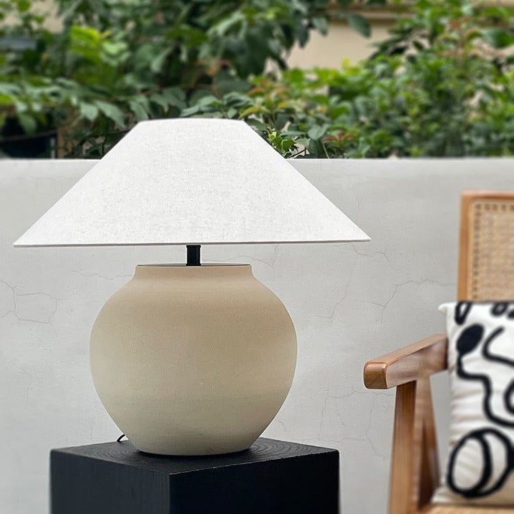 Front view of matte beige ceramic lamp on black plinth in daylight