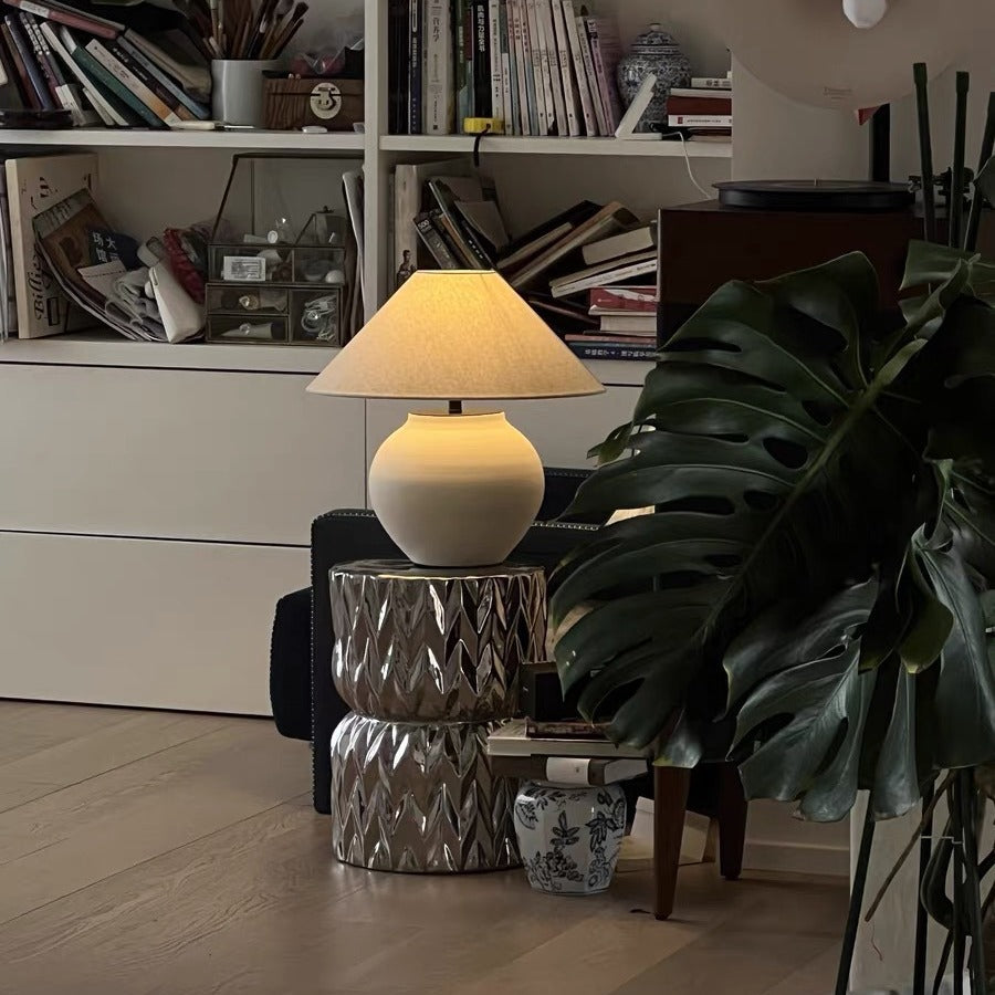 Illuminated ceramic lamp in a dimly lit study with books and plants
