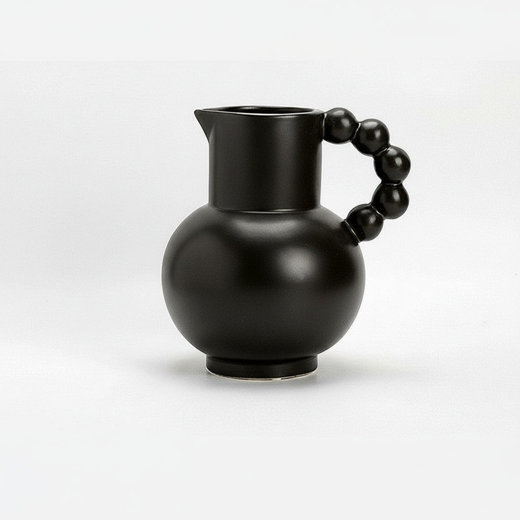 Matte black ceramic pitcher with beaded handle on a white surface