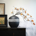 Matte black spherical vase with white textured band on sideboard