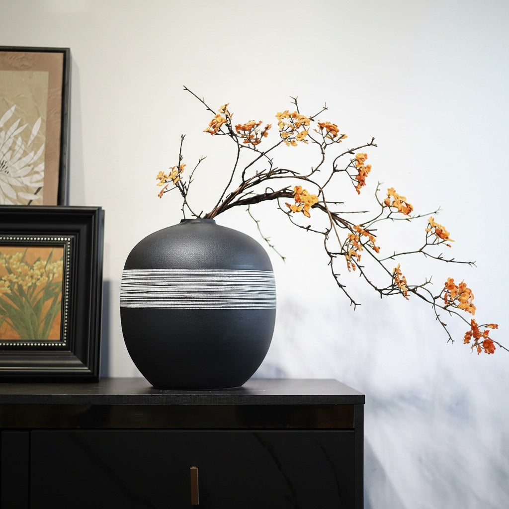 Matte black spherical vase with white textured band on sideboard
