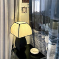 Matte black sculptural table lamp with linen shade on bedside table