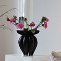 Matte black sculptural fluted vase with pink flowers on a white pedestal