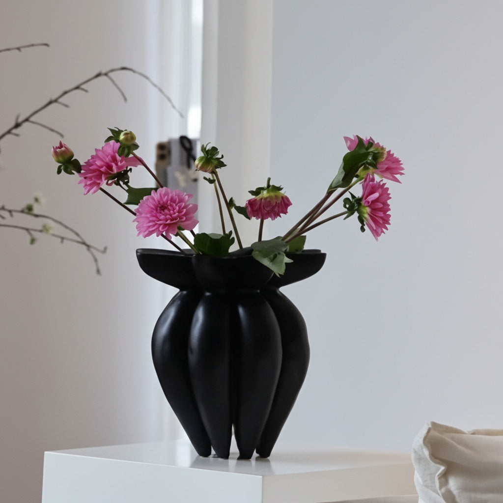Matte black sculptural fluted vase with pink flowers on a white pedestal