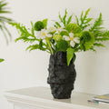 Matte black textured ceramic vase holding white flowers and greenery on a mantel