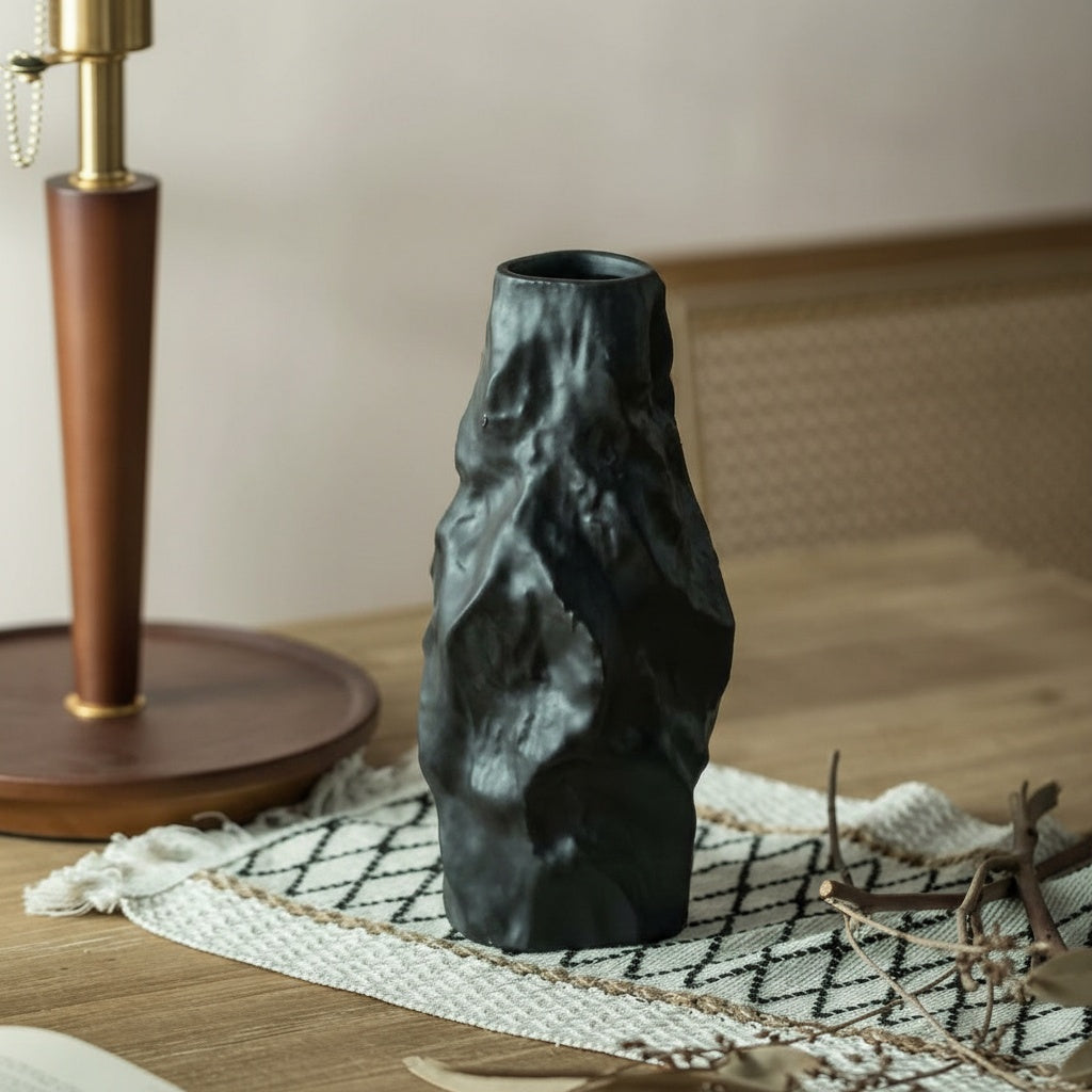 Matte black vase on woven mat next to wooden lamp base
