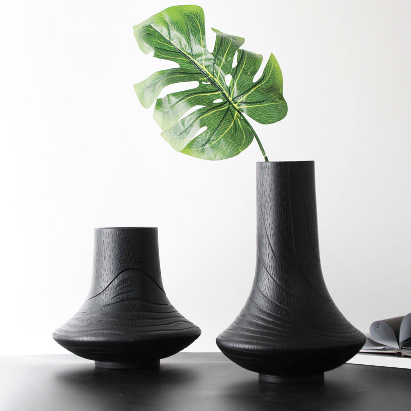 Two matte black textured vases on a table with green leaf