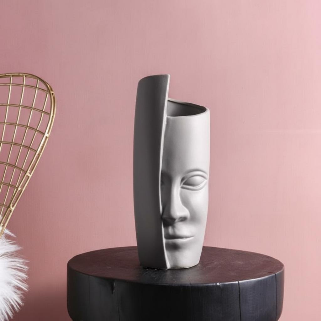 Front view of matte grey abstract face vase on black pedestal