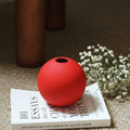 Matte red ceramic spherical bud vase on book with flowers