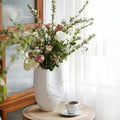 Matte white ceramic vase with botanical relief holding pink flowers