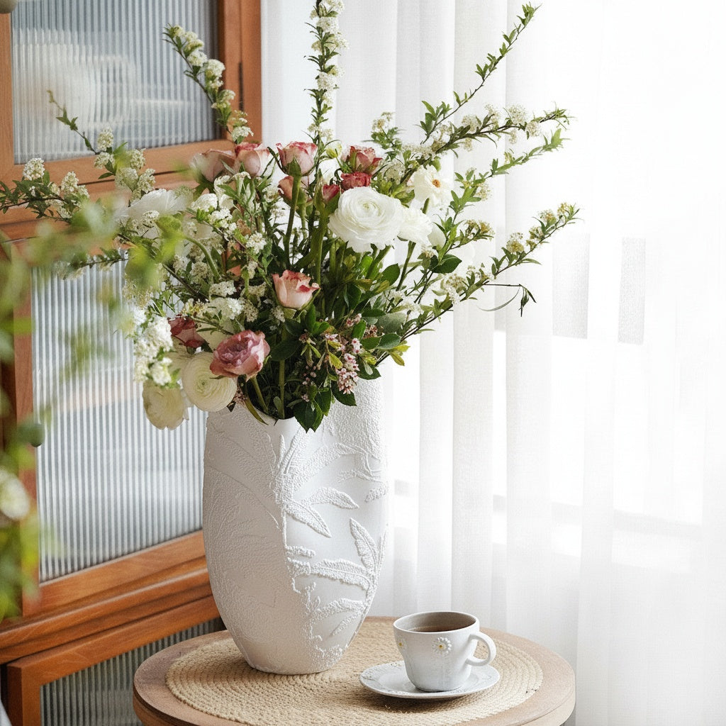 Matte white ceramic vase with botanical relief holding pink flowers