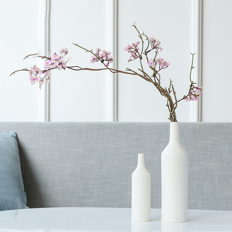 Matte white ceramic bottle vase with pink blossoms on table