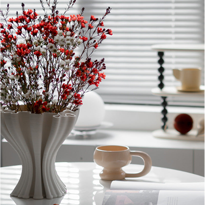 Matte white ceramic ruffled wave vase with red flowers on table