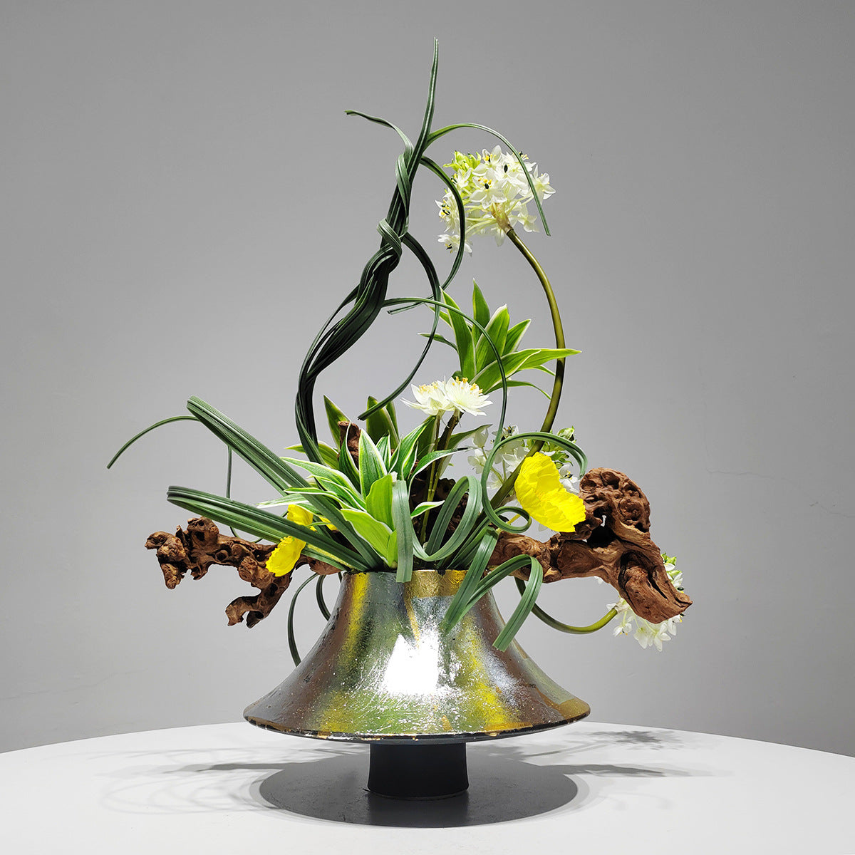 Detail of white artificial blooms and driftwood on metallic vase