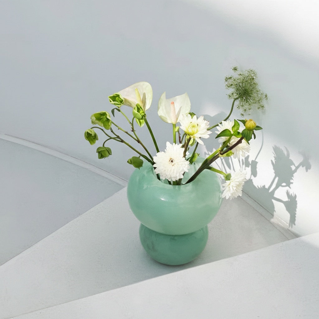 Mint green glass vase with white flowers on table
