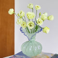 Mint green glass vase with blue ruffled rim holding yellow flowers