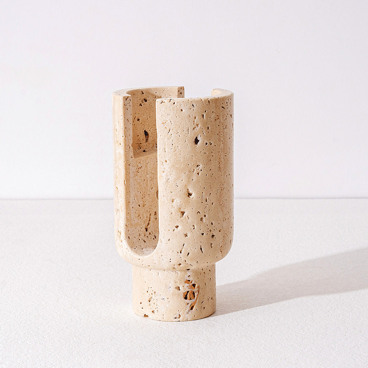 Full view of empty beige travertine candle holder showing pedestal base and vertical carved slots