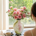 Mottled art glass vase styled with fresh pink roses on a sunlit table.