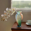 Multicolor art glass urn vase with white orchids on wooden table