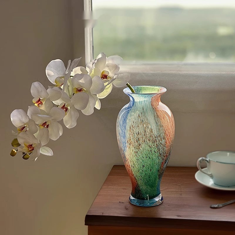 Multicolor art glass urn vase with white orchids on wooden table