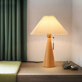 Natural wood conical table lamp with pleated shade lit in room