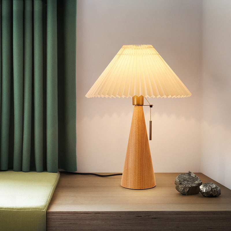 Natural wood conical table lamp with pleated shade lit in room