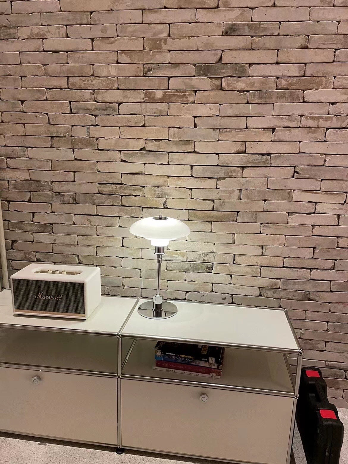 Chrome finish opal glass lamp on white cabinet against brick wall